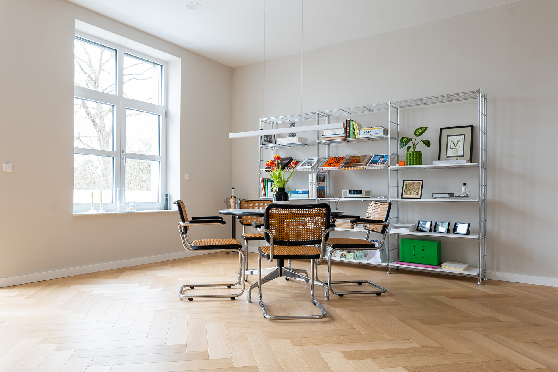 Parkett in Fischgrat mit rundem Tisch sowie passenden Stühlen und einem Regal mit Bildern und Büchern