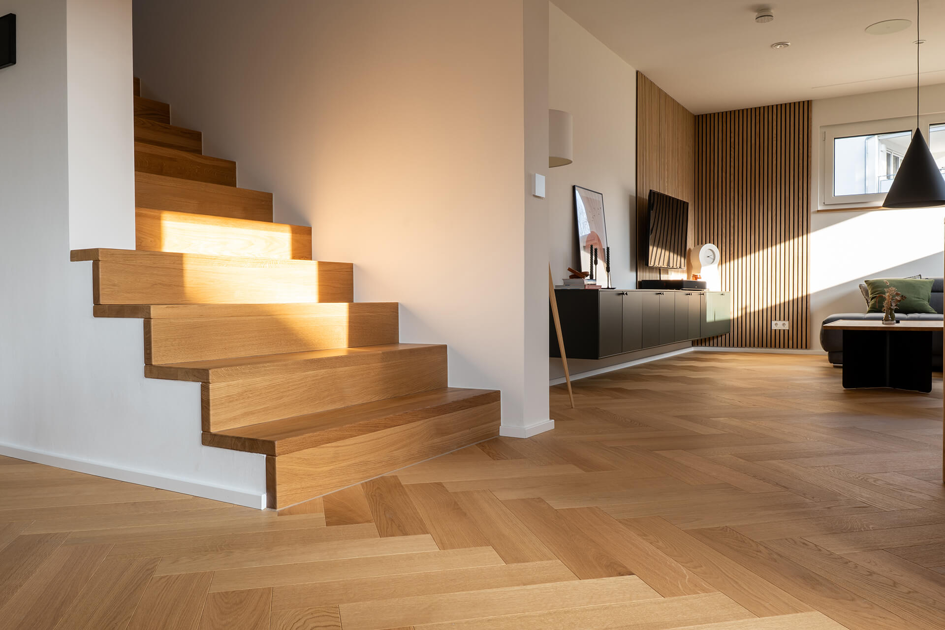 comfort-tabis-xl-eiche-elegance-geölt-fischgrat-3 Eichenholztreppe mit integrierter Beleuchtung und Übergang zum Fischgrat-Parkettboden im Erdgeschoss