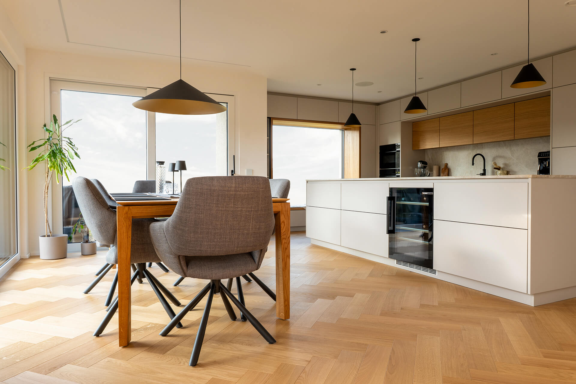 comfort-tabis-xl-eiche-elegance-geölt-fischgrat-5 Offener Wohn- und Essbereich mit Fischgratparkett aus Eiche Elegance, Kücheninsel und großen Fensterfronten