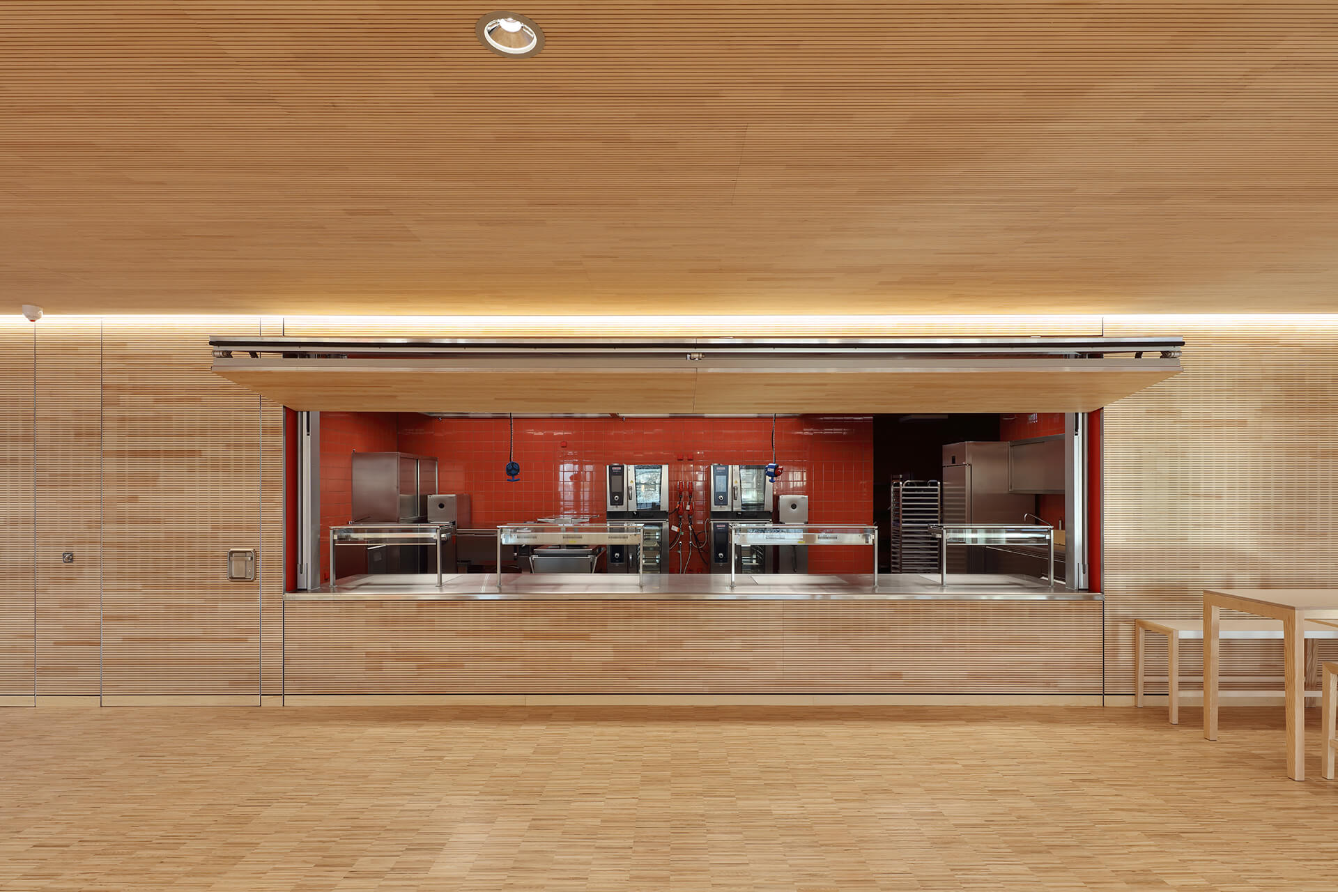 syrlin-grunschule-ulm-industrieparkett-esche-5 Küchenausgabe mit roter Fliesenrückwand und Eschenparkett im Erdgeschoss der Syrlin Grundschule Ulm