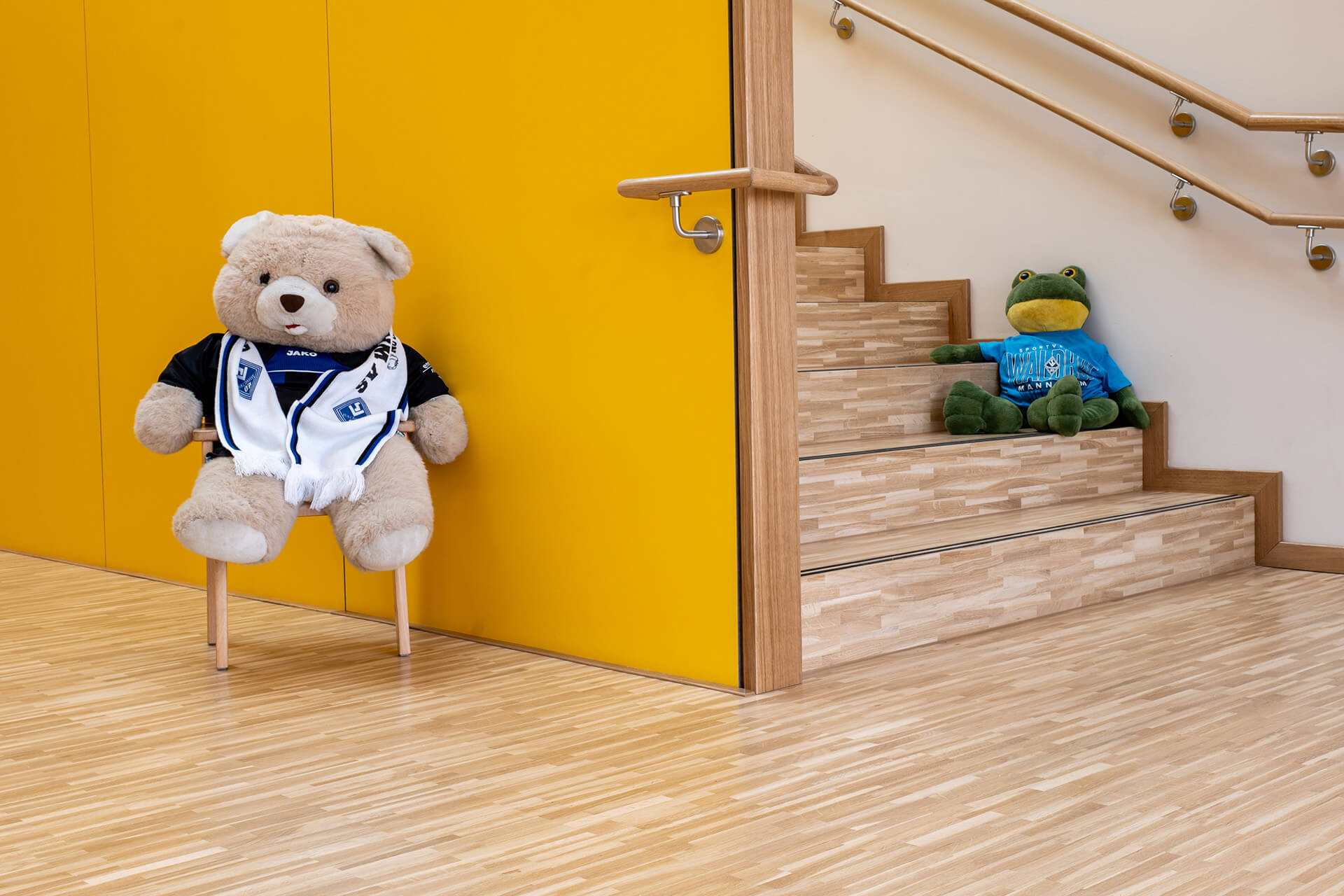 meisterparkett-eiche-gestreift-englischer-verband-kiga-ladenburg Teddybär und Plüschfrosch in SV Waldhof Mannheim Trikots auf Eichenparkett und Treppenstufen im Kindergarten St. Johannes Ladenburg bei Mannheim
